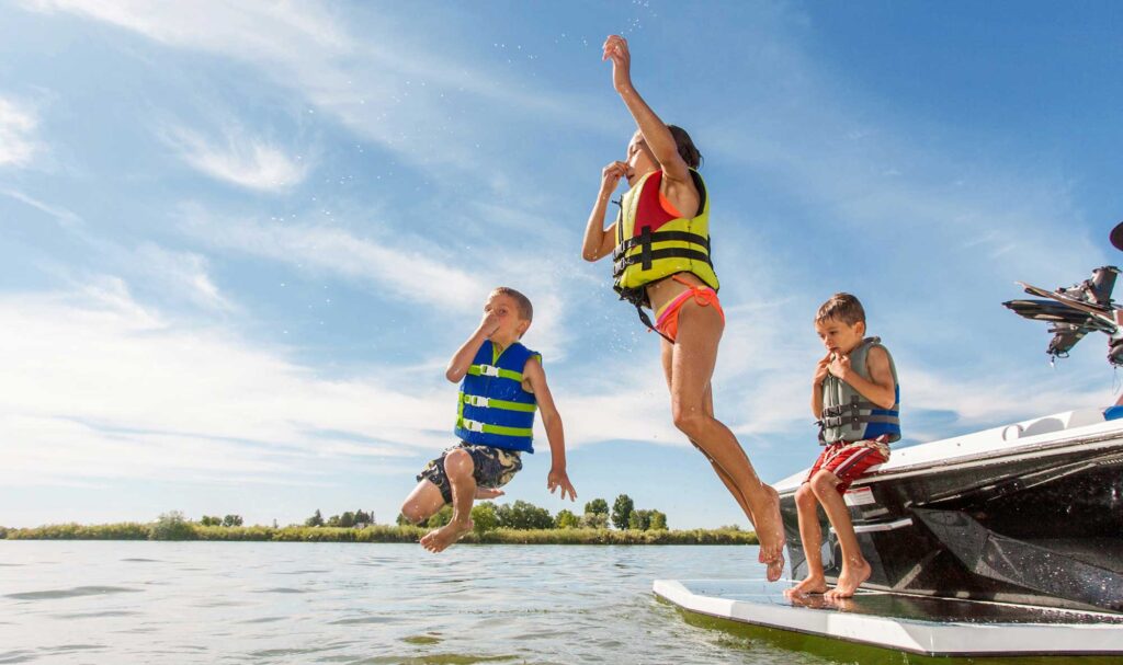 Children jumping off boat into lake wearing life jackets