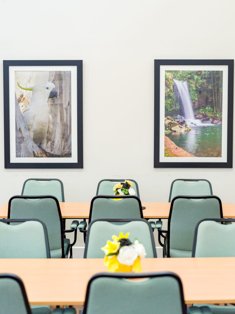 Framed resident photographs of a sulphur-crested cockatoo and a rainforest waterfall above the tables in the Clubhouse at Vantage Logan Village Links