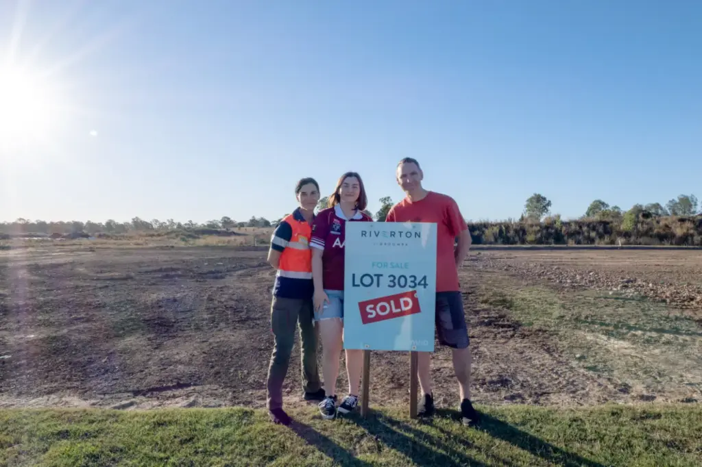 Three people beside sold land lot sign
